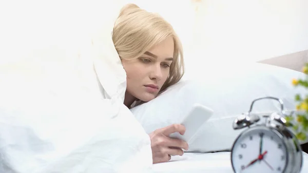 Awake woman using smartphone near retro alarm clock — Stock Photo