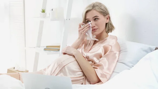 Sentimental blonde pregnant woman crying and wiping tears while watching movie on laptop — Stock Photo