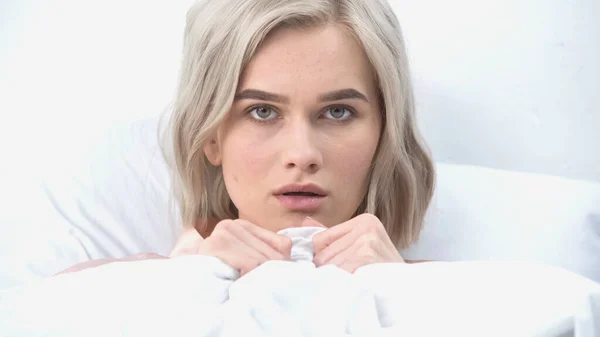 Joven mujer asustada cubriendo con manta en la cama - foto de stock