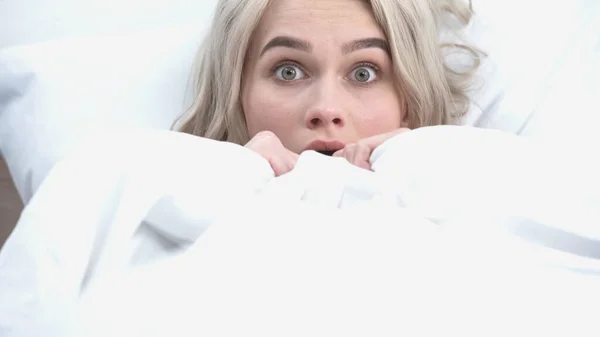 Young shocked woman covering with white blanket in bed — Stock Photo