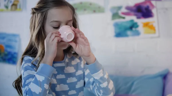 Preteen girl in pajama drinking tea in blurred bedroom — Foto stock