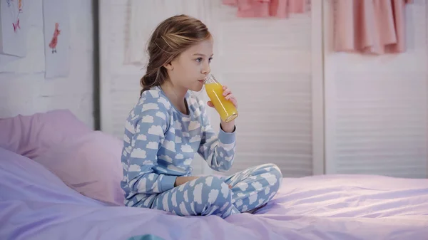 Preteen kid drinking orange juice on bed in evening — Fotografia de Stock