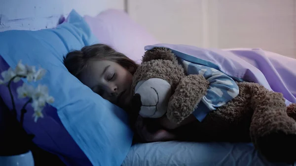 Preteen kid hugging soft toy while sleeping on bed at home — Stock Photo