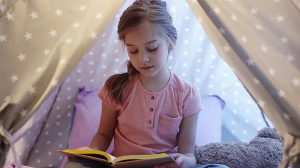 Preteen kid reading book in wigwam mit Beleuchtung zu Hause — Stockfoto