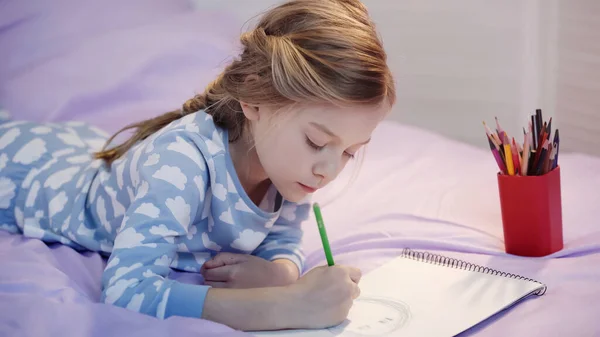 Preteen kid im Pyjama zeichnen auf Skizzenbuch auf dem Bett — Stockfoto