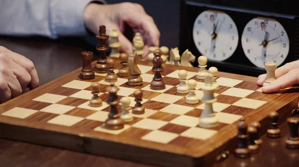Selective focus of chessboard with figures near cropped men playing at home — Stock Photo