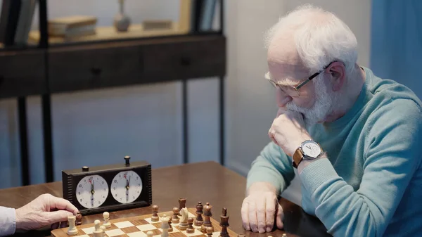 Pensive man looking at chessboard while gaming with senior friend at home — Foto stock