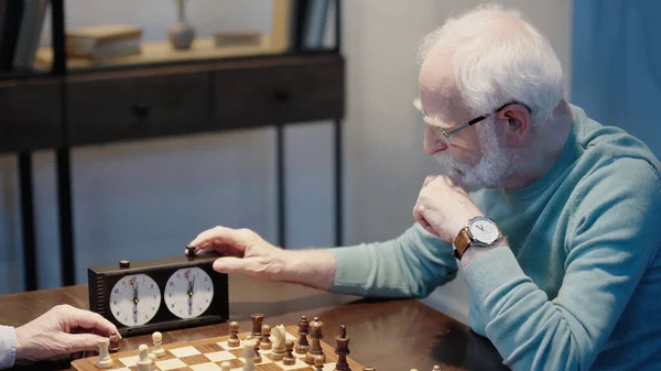 Bearded man fixing time on chess clock while gaming with senior friend at home — Foto stock