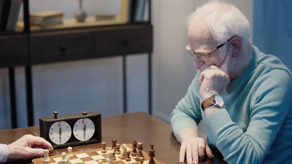 Grey haired man in eyeglasses thinking near chessboard and senior friend — стоковое фото
