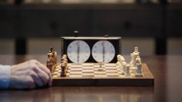 Selective focus of chessboard near cropped man and blurred chess clock — Stock Photo