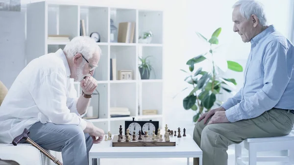 Вид збоку вдумливого чоловіка, який грає в шахи з старшим другом у вітальні — стокове фото