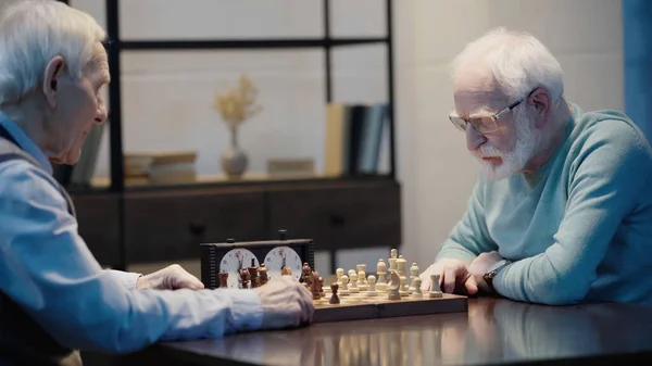 Thoughtful man in eyeglasses playing chess with senior friend — Foto stock