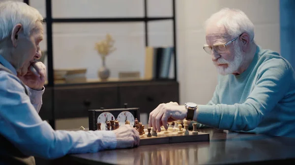 Bearded man in eyeglasses playing chess with thoughtful friend at home — стоковое фото