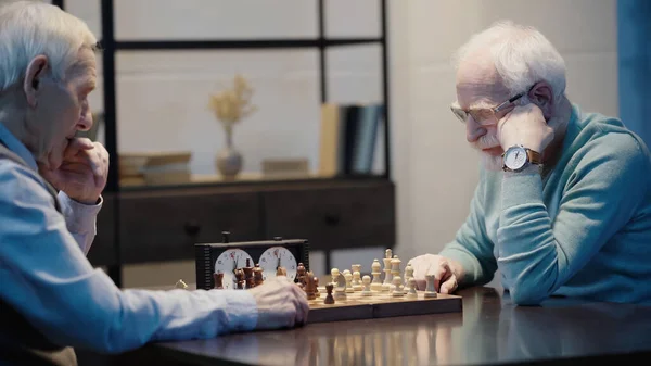 Pensive senior man playing chess with friend at home — Photo de stock