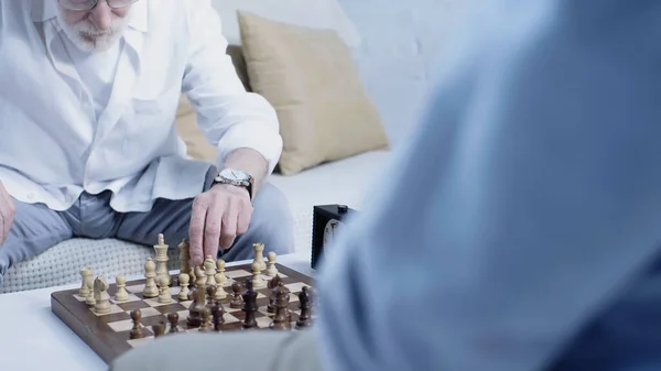 Обрізаний вид на старшого чоловіка біля шахівниці і розмитого друга — стокове фото