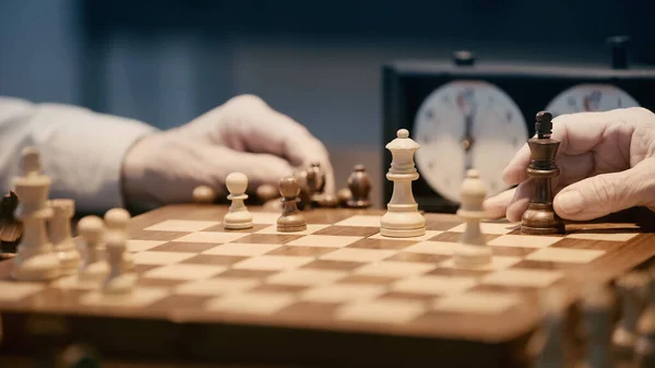 Partial view of senior men playing chess on blurred chessboard — Stock Photo