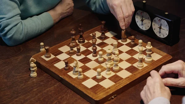 Частковий погляд на чоловіка, який рухає фігуру в шахи, граючи з старшим другом — стокове фото