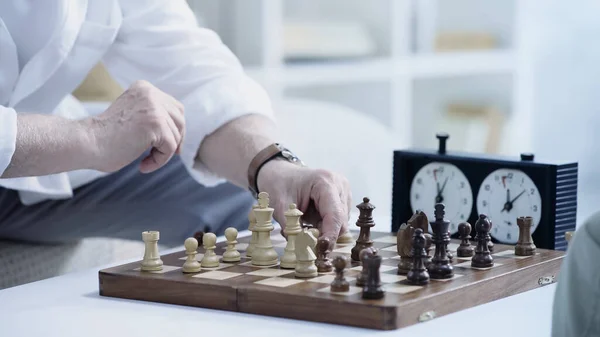 Cropped view of senior man moving chess figure while gaming at home — Stock Photo