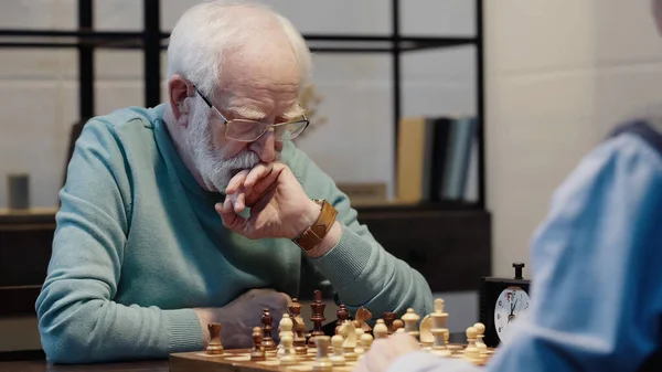 Thoughtful grey haired man playing chess with senior friend at home — Photo de stock