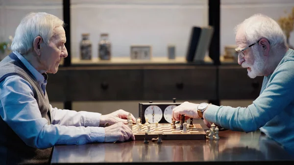 Side view of senior grey haired men playing chess in living room — Foto stock