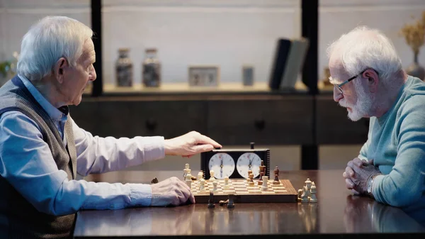 Side view of grey haired man fixing time on chess clock near senior friend — Stock Photo