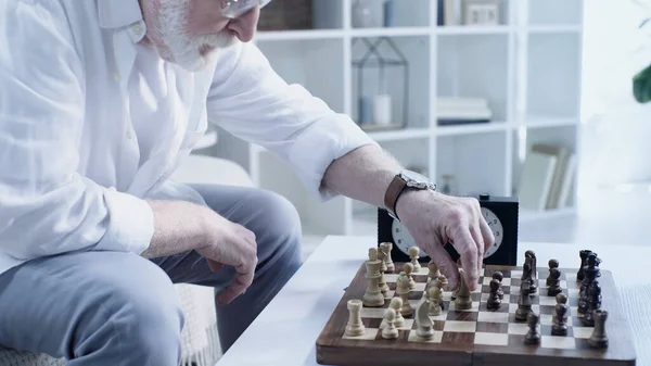 Partial view of senior bearded man playing chess at home in living room — Stockfoto