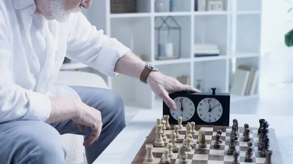 Cropped view of senior man using timer near chessboard at home — Foto stock