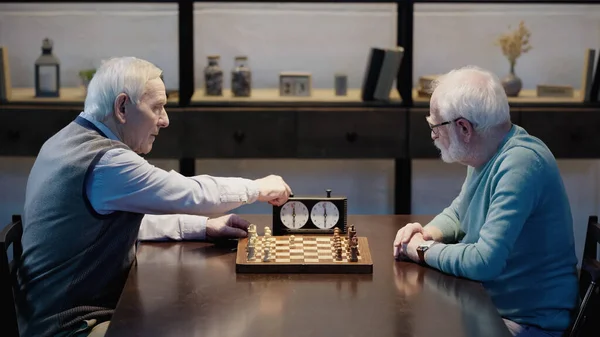 Side view of grey haired man fixing time on chess clock near senior friend — Stock Photo