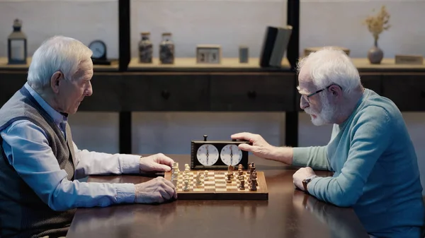 Вид збоку на ігри старшого чоловіка з другом, що фіксує час на шаховому годиннику — стокове фото