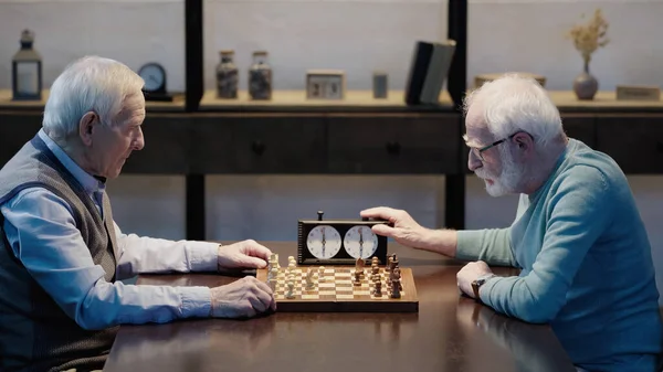 Side view of senior man gaming with friend fixing time on chess clock — Stock Photo