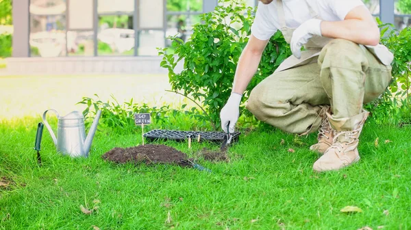 Cropped view of gardener in gloves holding shovel near soil and watering can in garden — Fotografia de Stock