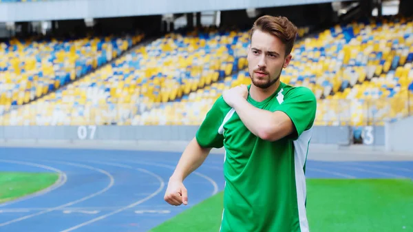 Young football player in green t-shirt warming up on stadium — Stockfoto