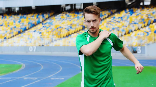 Bearded football player in t-shirt touching shoulder while warming up on stadium — Foto stock