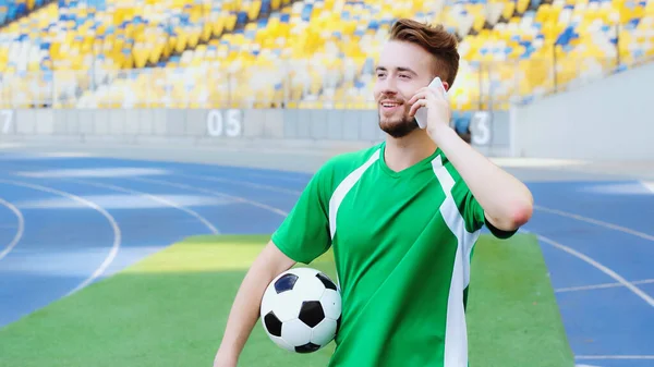 Smiling football player holding ball and talking on smartphone — Stock Photo