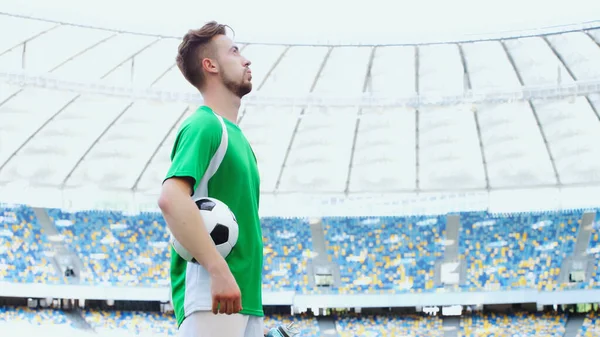 Side view of young football player in green t-shirt breathing while holding ball — Foto stock