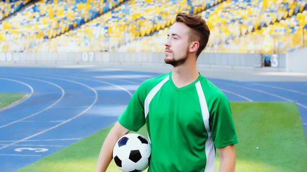 Bearded sportsman in uniform holding soccer ball and looking away — стоковое фото