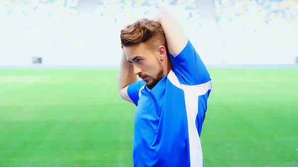 Bearded football player in blue t-shirt warming up on green field of stadium - foto de stock