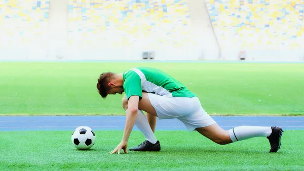 Young football player in uniform stretching legs on green grass bear soccer ball — стоковое фото