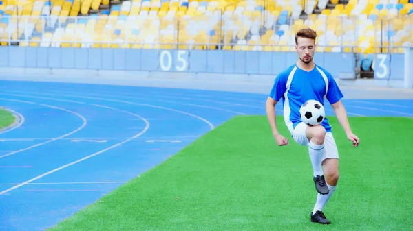 Young football player bouncing soccer ball with legs on stadium — Stockfoto