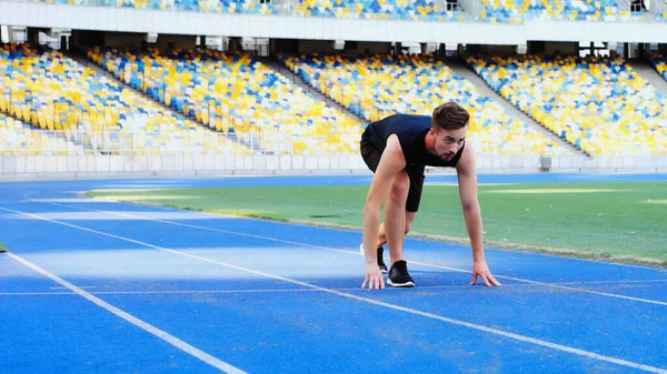 Bearded man in sportswear standing at starting pose before running at stadium — Foto stock