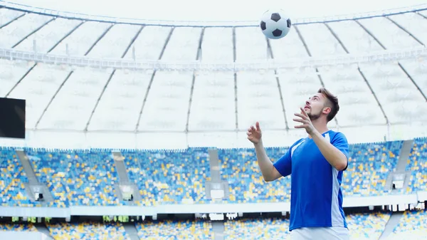 Sportive football player in blue uniform bouncing ball with head on stadium — Stockfoto