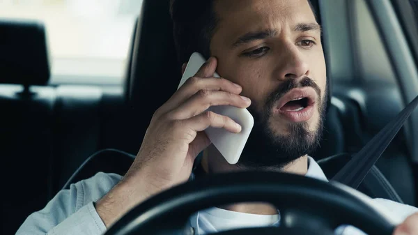 Surprised man talking on smartphone while driving car - foto de stock