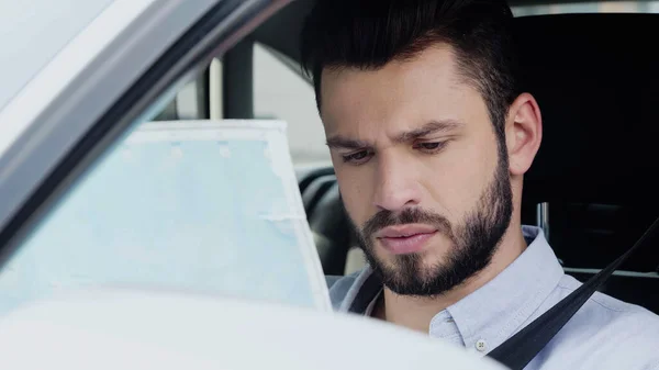 Young and thoughtful man estimating location while sitting in car and looking at map — Fotografia de Stock