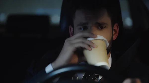 Бізнесмен водить машину вночі і п'є каву, щоб піти — стокове фото