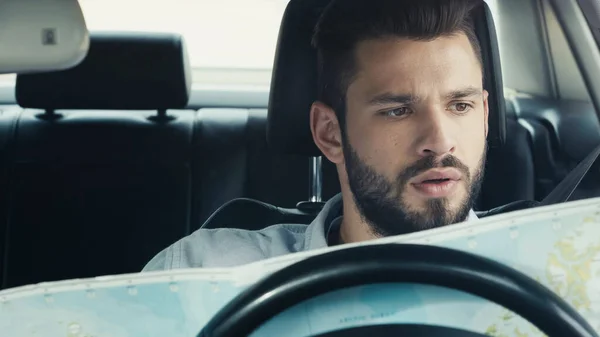 Thoughtful bearded man looking at map while sitting in car — Stock Photo
