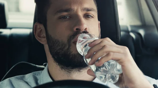 Young man driving car and drinking fresh water from plastic bottle — Photo de stock