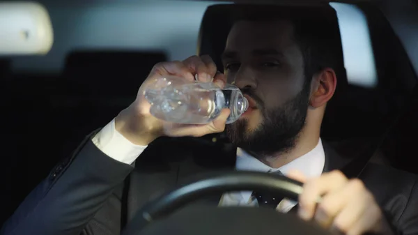 Thirsty businessman driving car and drinking pure water from plastic bottle — Photo de stock