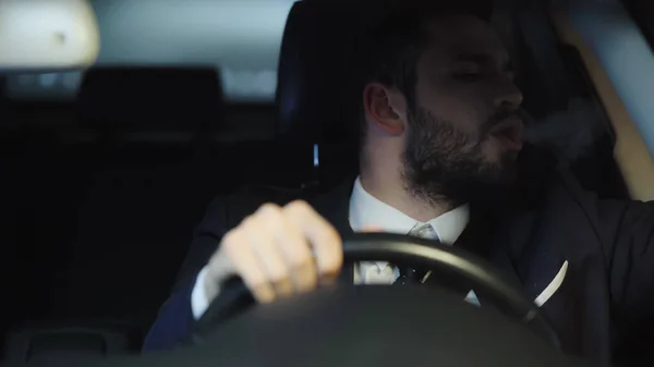 Man in formal wear smoking while driving car in evening — Stock Photo