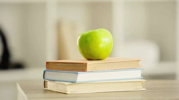 Green and fresh apple on stack of books on wooden desk — Stock Photo