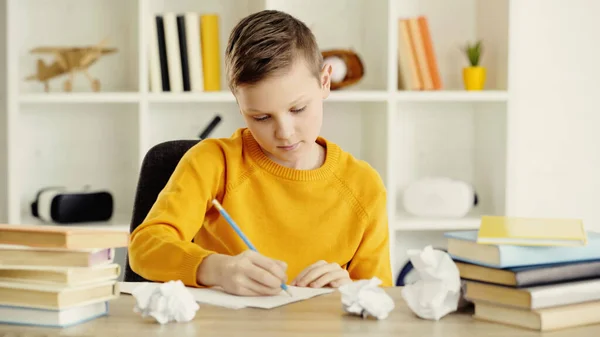 Preteen schoolboy drawing near crumpled papers and books on desk — стоковое фото